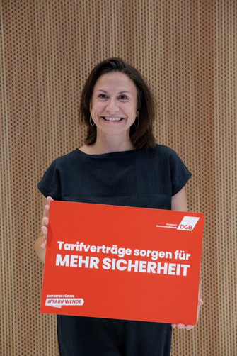 Portraitfoto von Lisi Maier, Direktorin der Bundesstiftung Gleichstellung, die ein Plakat in den Händen hält mit der Aufschrift "Tarifverträge sorgen für mehr Sicherheit".