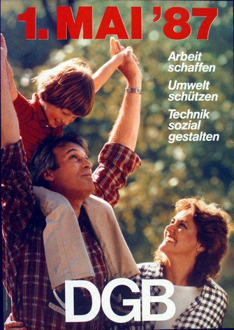 Maiplakat 19987. Text "Slogan 1987 "1. Mai '87. Arbeit schaffen – Umwelt schützen –  Technik sozial gestalten". Motiv: Eine dreiköpfige Familie im Grünen, der Vater trägt seinen etwa vierjährigen Sohn auf der Schulter und hält ihn an den Armen. Die Mutter schaut lächelnd zum Kind.