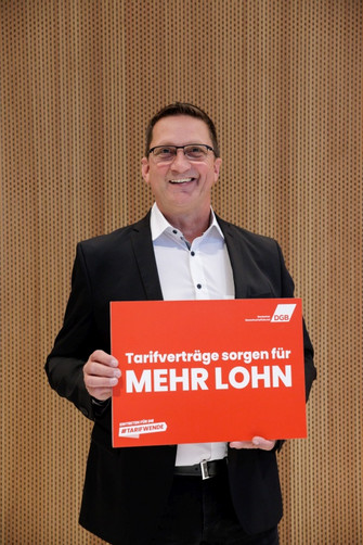 Portraitfoto von Joachim Noll, Arbeitnehmer-Vizepräsident des Deutschen Handwerkskammertages, der eine Plakat hält mit der Aufschrift "Tarifverträge sorgen für mehr Lohn".