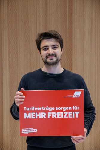 Portraitfoto von Jan Dieren (SPD-Abgeordneter im Deutschen Bundestag), der ein Plakat in der Hand hält mit der Aufschrift "Tarifverträge sorgen für mehr Freizeit". 