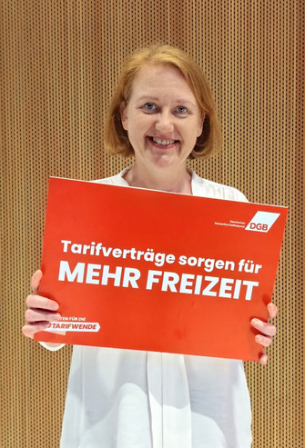 Foto von Lisa Paus (Bündnis 90/Die Grünen), die ein Plakat hält mit der Aufschrift "Tarifverträge sorgen für mehr Freizeit". 