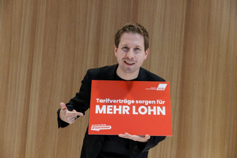 Portraitfoto von Kevin Kühnert, Generalsekretär der SPD, der ein Plakat hält mit der Aufschrift  "Tarifverträge sorgen für mehr Lohn". 