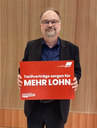 Portraitfoto von Lukas Siebenkotten, Präsident des Deutschen Mieterbunds, der ein Plakat in den Händen hält mit der Aufschrift "Tarifverträge sorgen für mehr Lohn". 