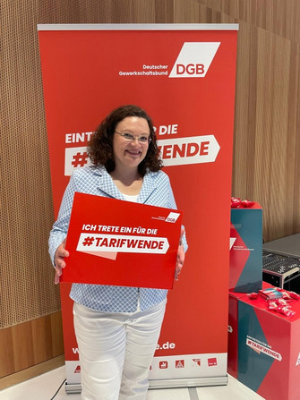 Portraitfoto von Andrea Nahles, Vorstandsvorsitzende der Bundesagentur für Arbeit, die ein Plakat hält mit der Aufschrift "Ich trete ein für die #Tarifwende". 