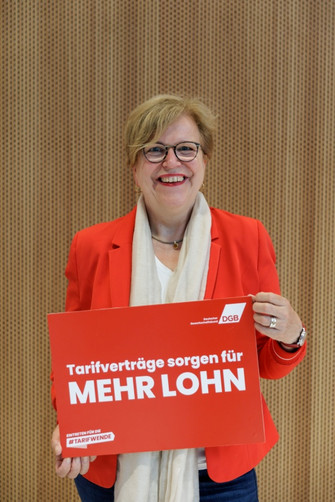 Portraitfoto von Gaby Bischoff, die ein Plakat in der Hand hält mit der Aufschrift "Tarifverträge sorgen für mehr Lohn". 