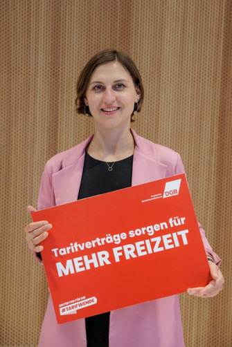 Portraitfoto von Janina Henkes, die ein Plakat in den Händen hält mit der Aufschrift "Tarifverträge sorgen für mehr Freizeit". 