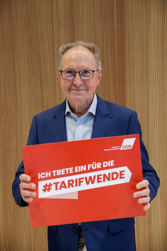 Portraitfoto von Jörg Cezanne (Die Linke), der ein Plakat hält mit der Aufschrift "Ich trete ein für die #Tarifwende".